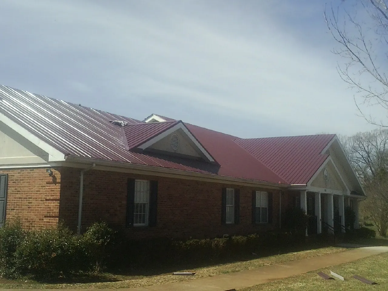 Red metal roof with gabled entries on a long brick building, from a Hail Damage Roof Repair job in Selbyville