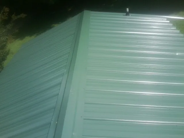 New green metal panels meeting at the ridge of a roof — Flat Roof Repair work by our crew in Selbyville