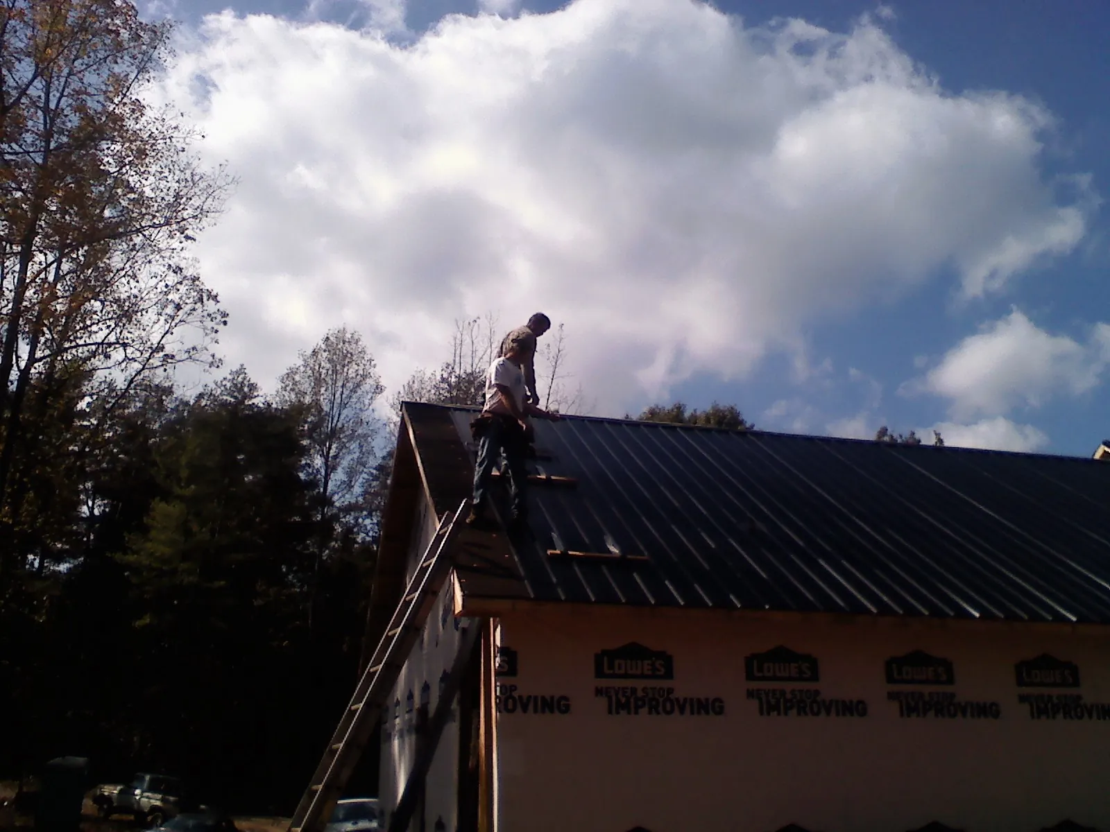 Roofer fastening dark metal panels high against a cloudy sky, from a Roof Inspection job in Selbyville