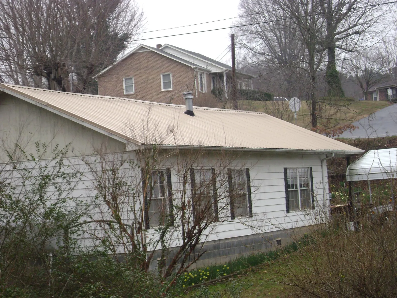 Tan metal roof on a white sided house set into a hillside — Commercial Roofing by Roofing Brothers in Selbyville